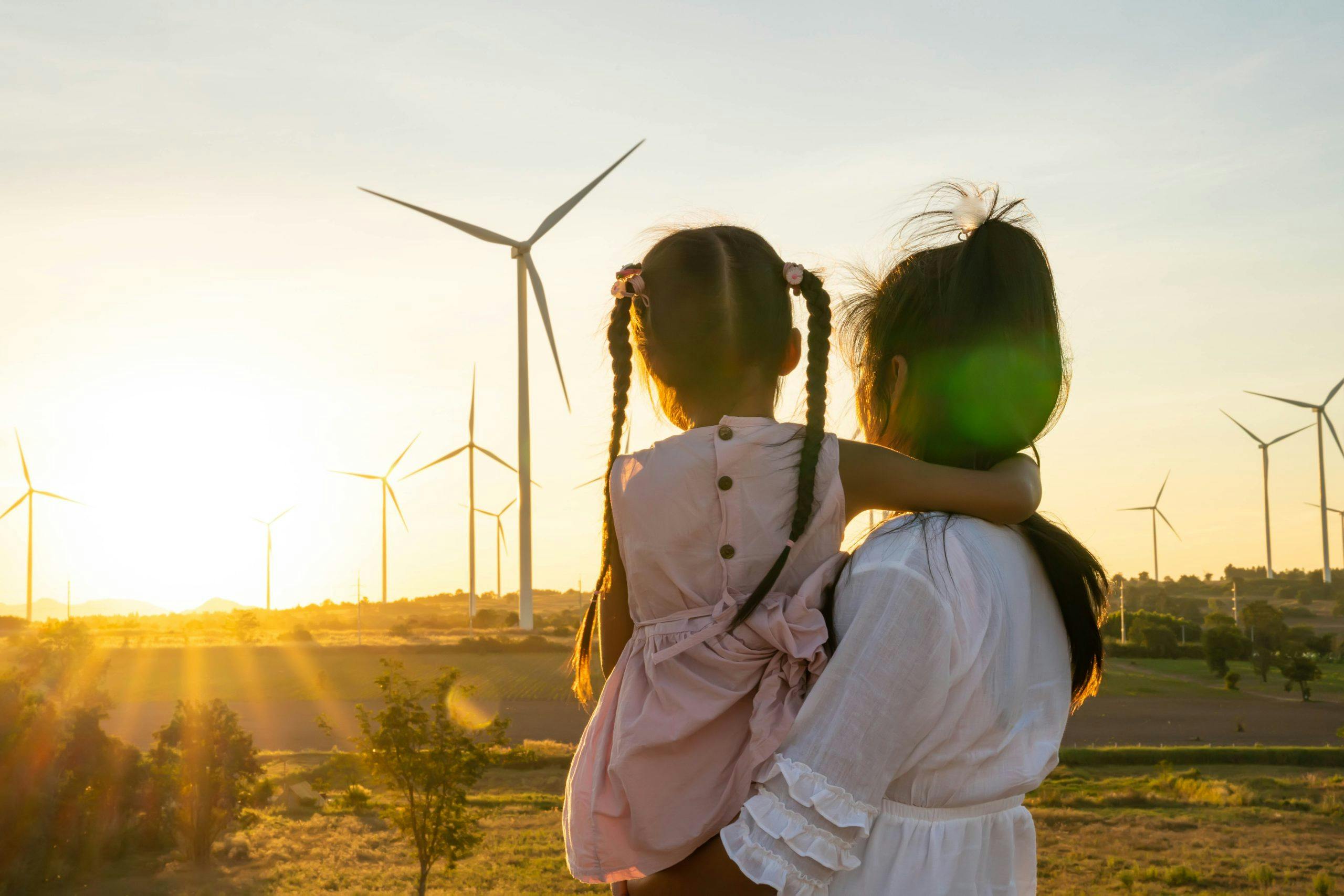 woman holding child, looking at wind turbine on field