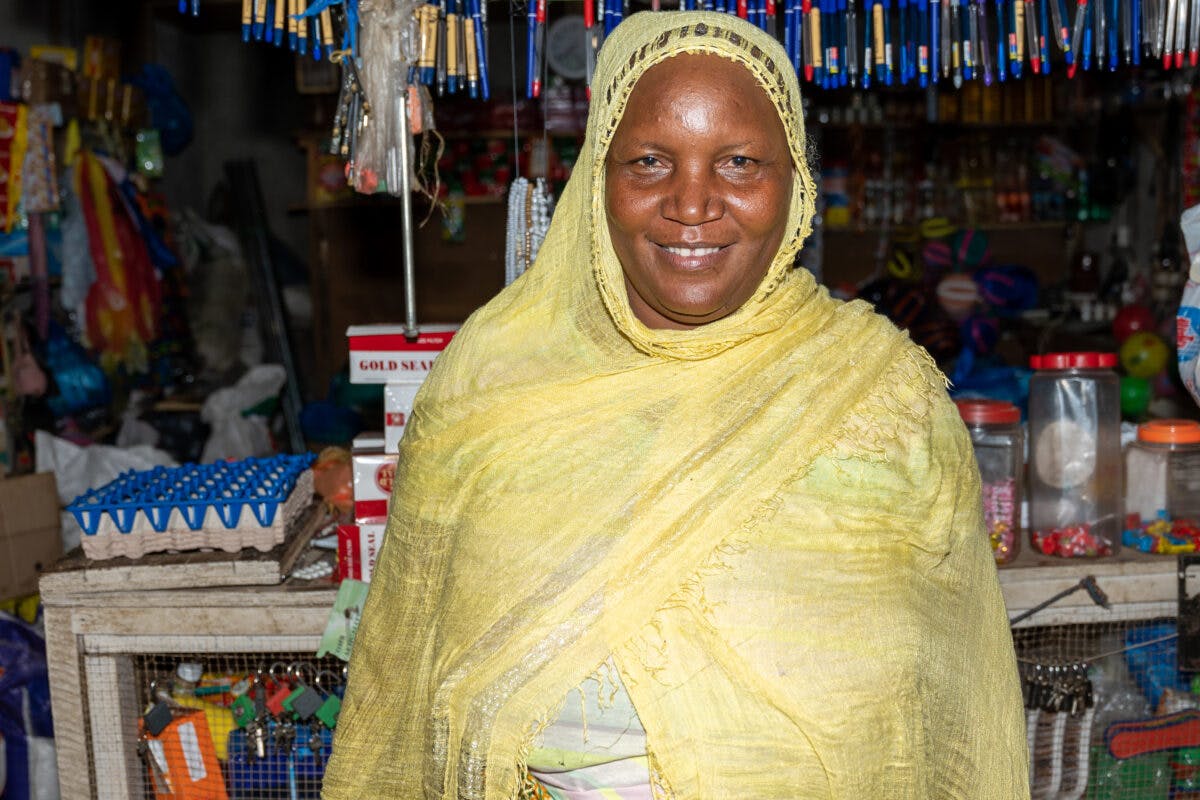 African woman in traditional wear smiling in front of market stall